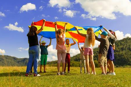 Quelle: unsplash.com/@artem_kniaz, https://unsplash.com/de/fotos/gruppe-von-frauen-die-tagsuber-auf-grunem-rasen-stehen-DqgMHzeio7g eine Gruppe Kinder steht im Kreis mit einem bunten Tuch